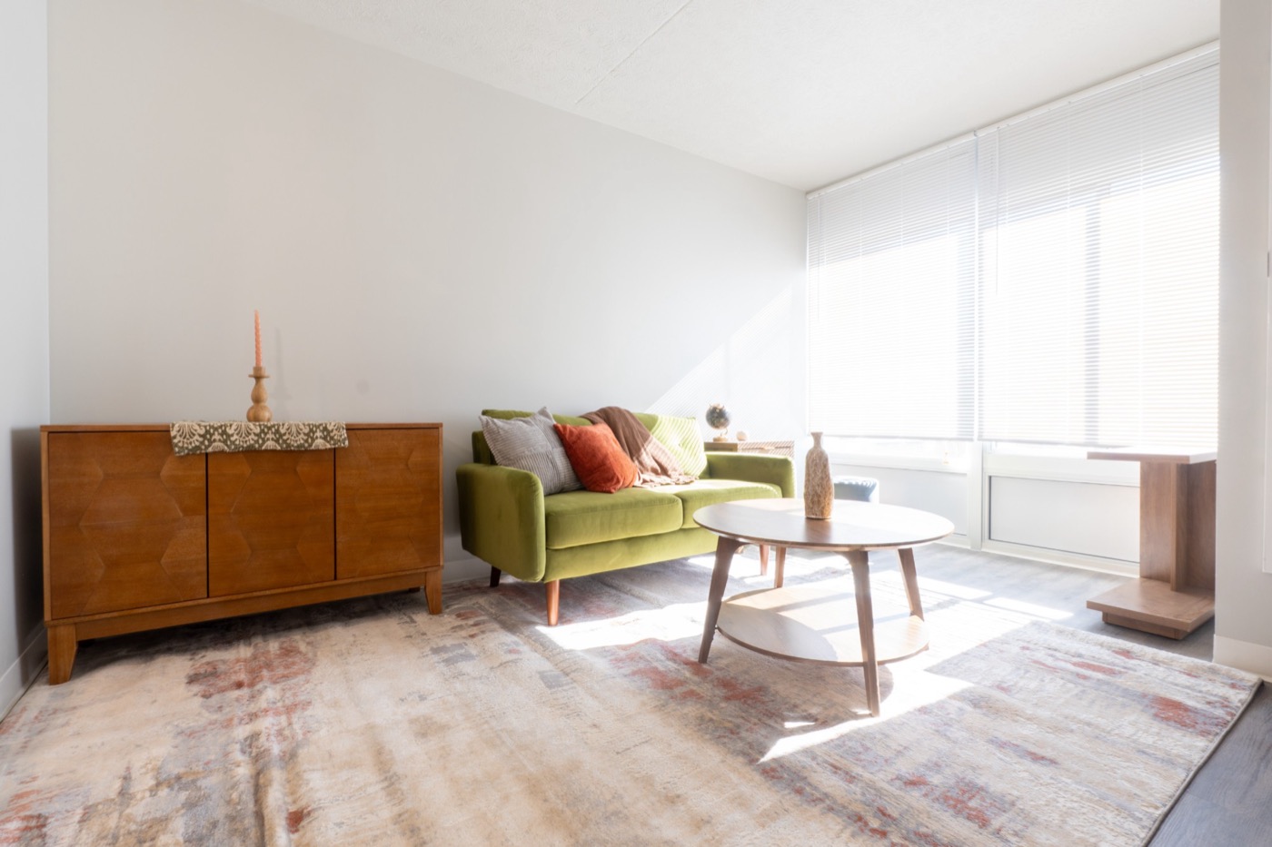 Living room staged by Design Domain with a green velvet loveseat, walnut credenza, and round coffee table